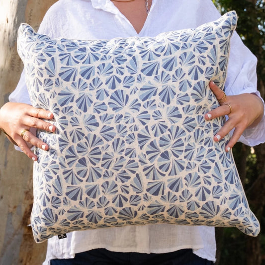 Woman holding square Pacific Shells linen cushion cover in blue and natural coastal tones