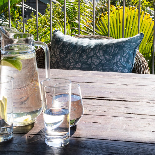 Outdoor dining setting with a Frenchmans colourway Pipi pattern lumbar cushion behind a rustic