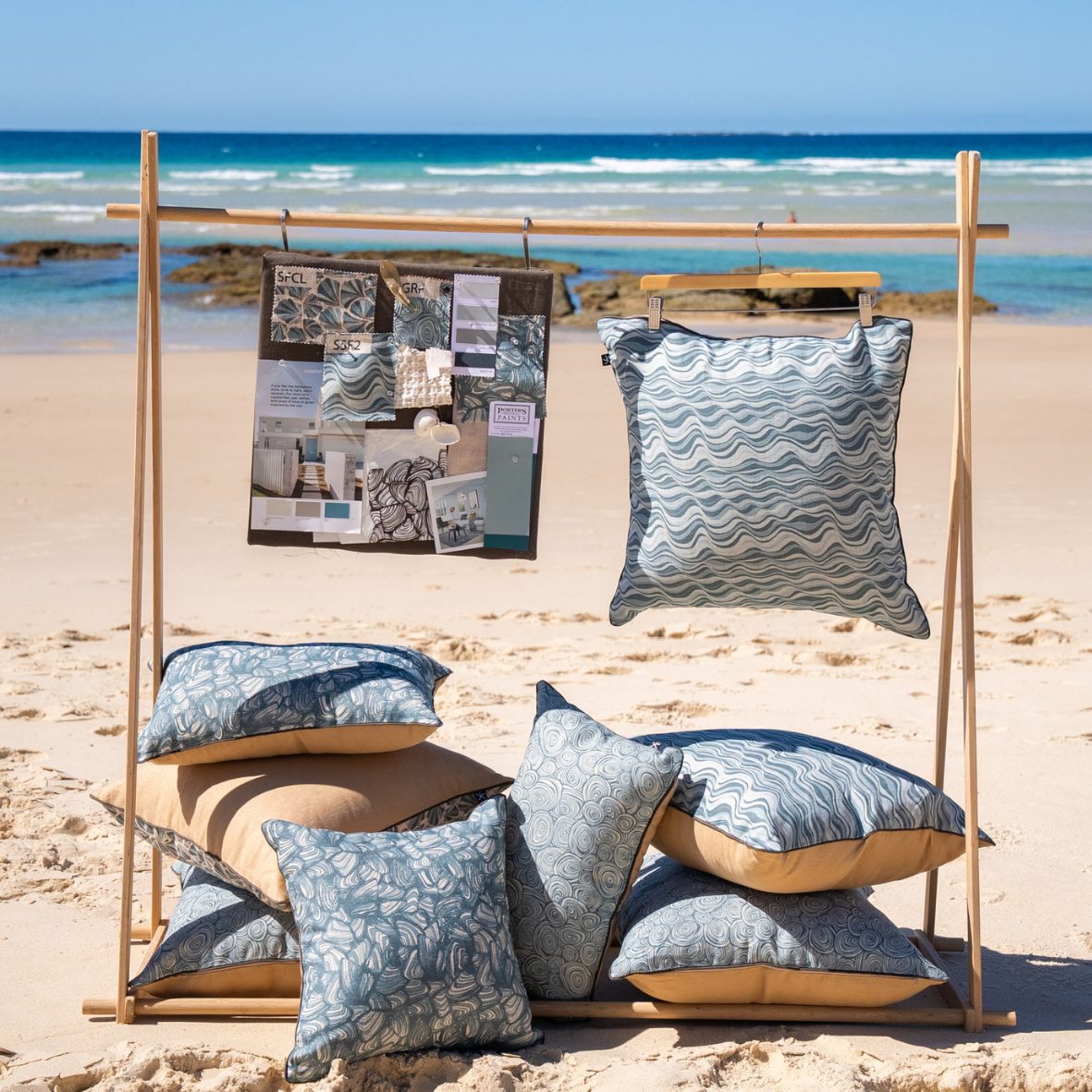 Frenchmans Pipi linen cushion covers displayed on a wooden stand on the beach with a styling mood board.