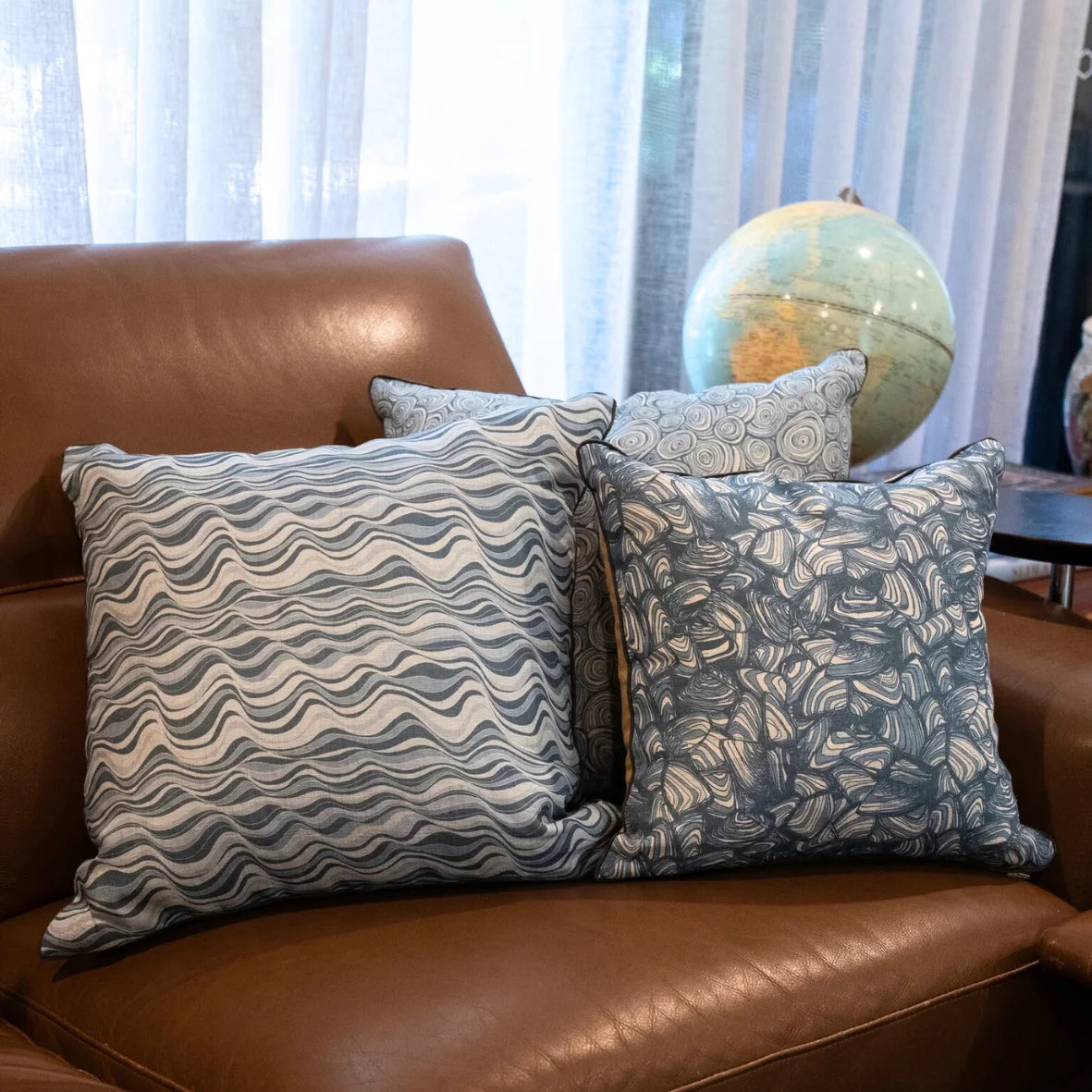 Frenchmans Straddie Stripe and Pipi linen cushion covers styled together on a brown leather sofa.