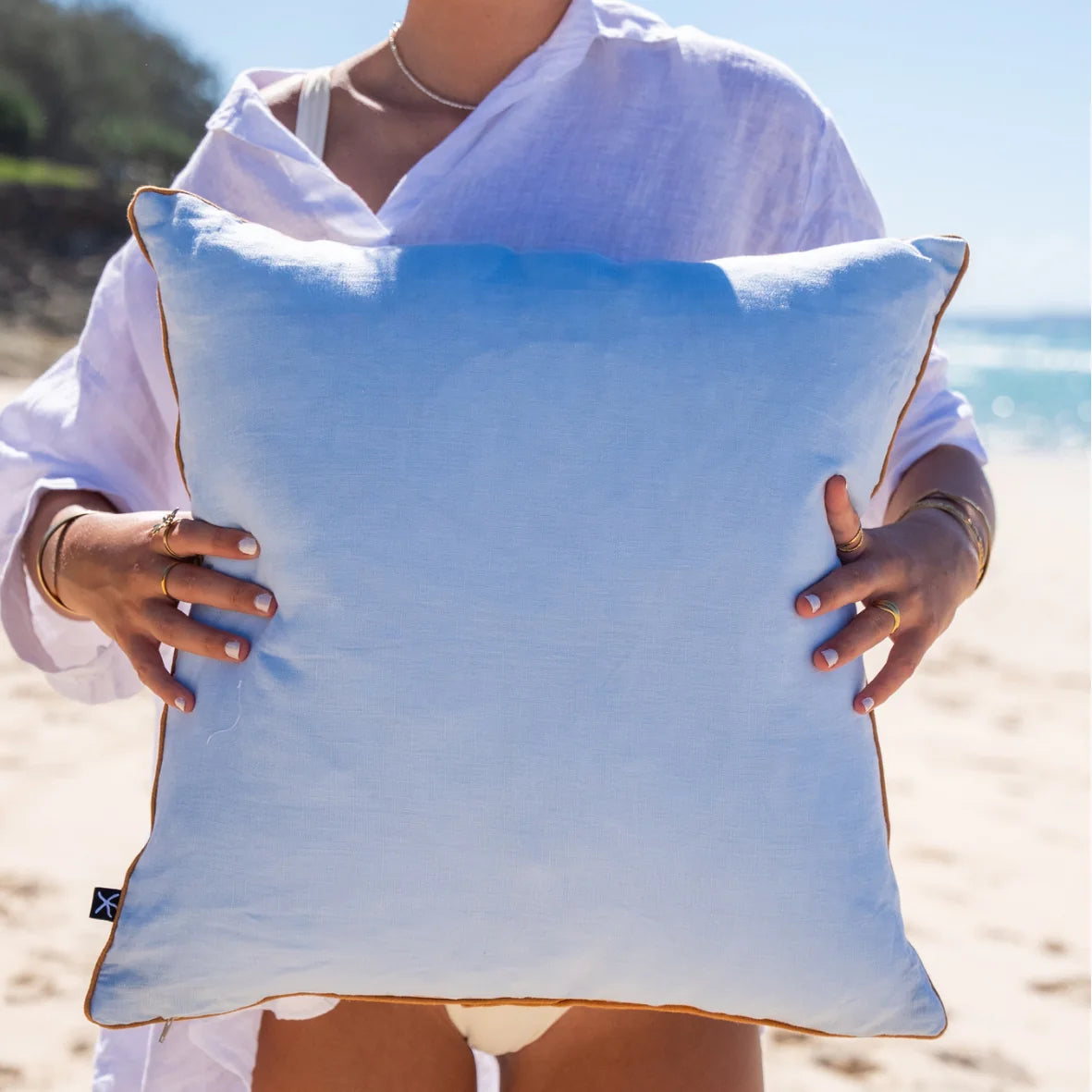 Back of the Shells linen cushion cover showing the plain pale blue linen reverse and orange piping.