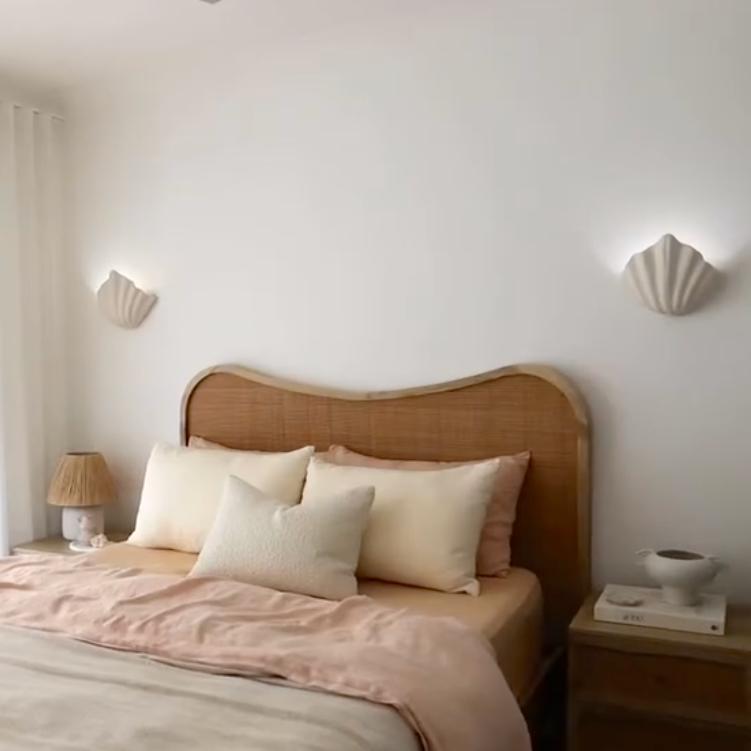 Bedroom with a wooden headboard and pink bedding, featuring two wall sconces.