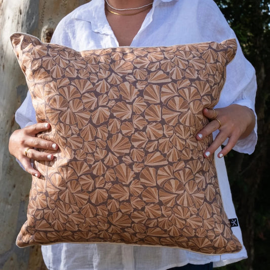 Woman holding square Claytons Shells linen cushion cover in warm earthy tones