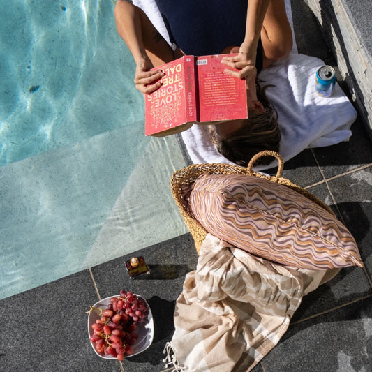 Claytons colourway Straddie Stripe cushion styled poolside with a woven bag, towel and grapes.