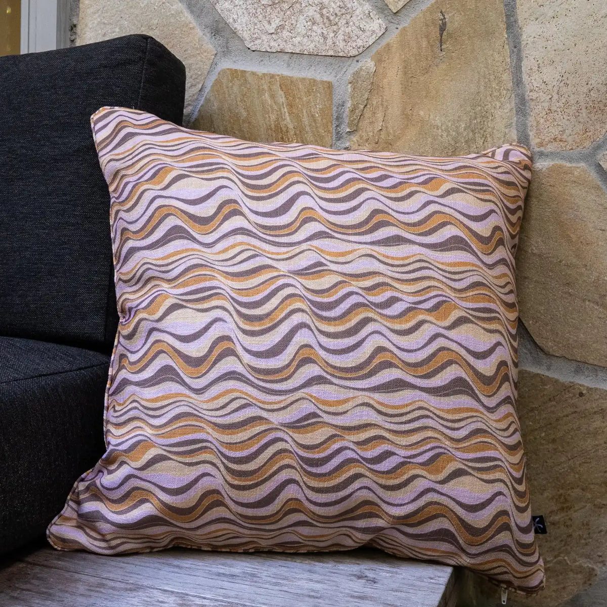 Claytons Straddie Stripe outdoor indoor cushion cover in a square size styled on an outdoor chair beside a stone wall.