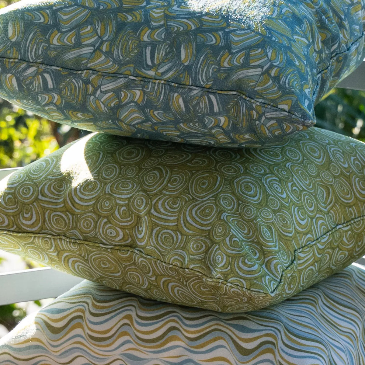 Close-up of the Outdoor Indoor Growth Rings cushion cover in Mangrove fabric, stacked with a teal swirl print cushion