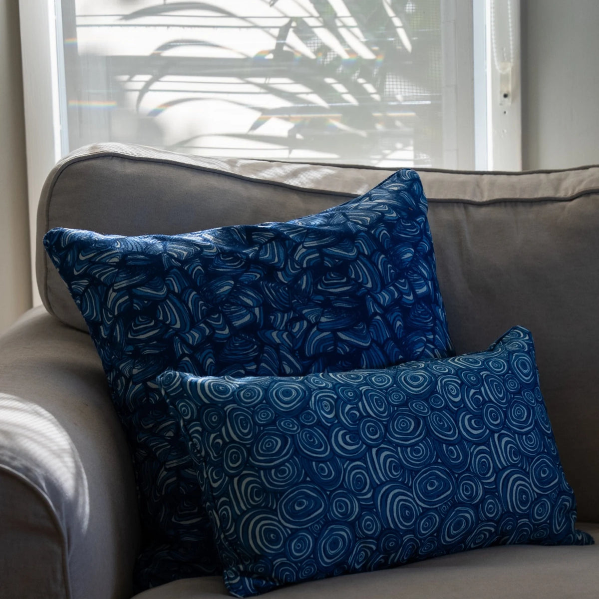 Ocean Growth Rings outdoor indoor cushion cover styled behind a coordinating blue print cushion on a timber armchair.