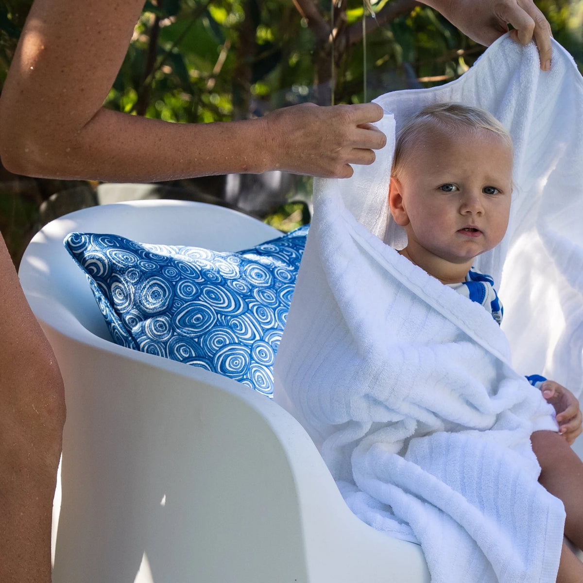 Ocean Growth Rings outdoor indoor cushion cover styled on a white pool chair behind a baby wrapped in a towel.