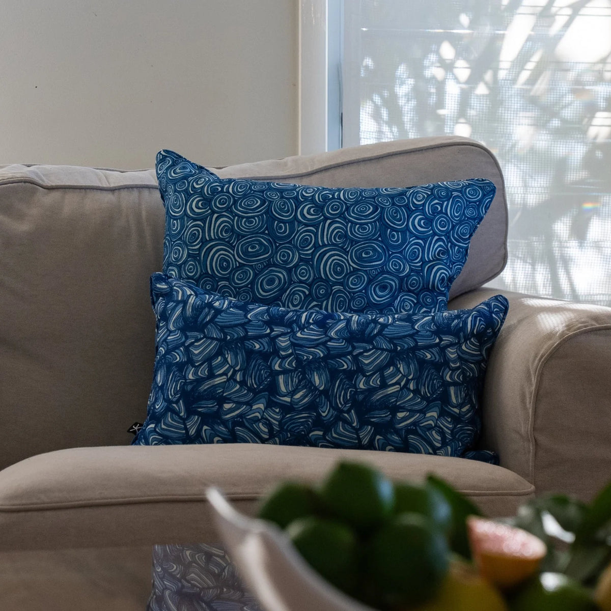 Ocean Growth Rings outdoor indoor cushion cover styled with a coordinating blue print cushion on a neutral sofa.