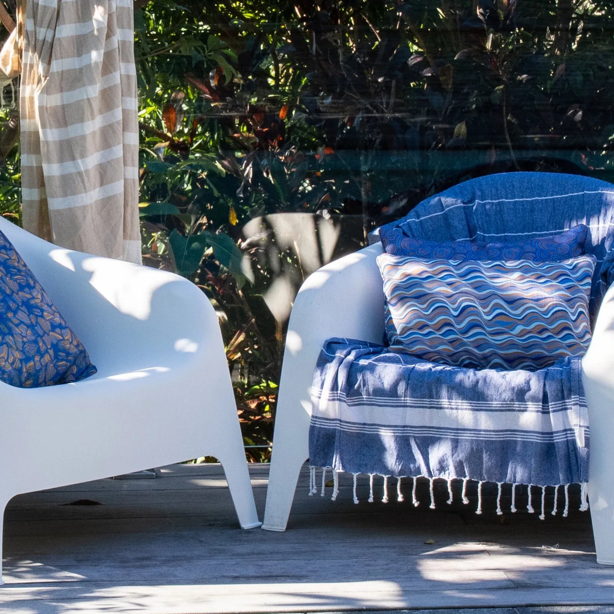 Outdoor seating area with white poolside chairs styled with patterned cushions and blue striped throws.